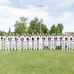 The 2023 Redding Colt 45s team standing two rows deep, in the shallow outfield, with the right-center field wall in the background.